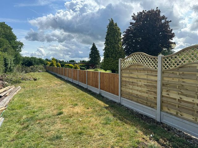 A long run of fence panels with curved trellis tops along a grassy field boundary