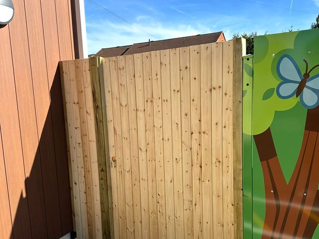 A tall pine gate fitted between a building and a painted mural panel