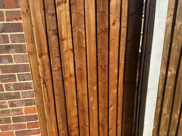 A closeboard gate in a timber frame between a brick wall and a concrete post