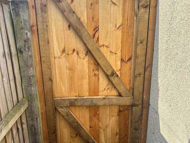 The braced inside face of a timber side gate with galvanised hinges and a bolt
