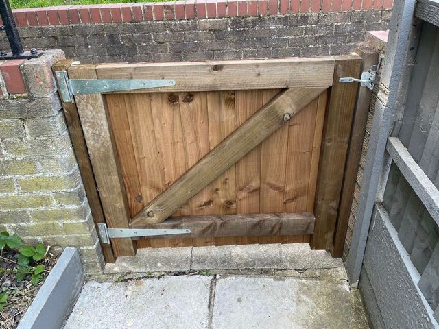 A low braced timber gate hung between a brick wall and a fence